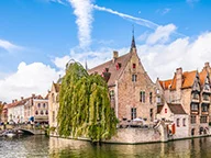 Vue pittoresque d'un canal bordé de maisons anciennes avec un ciel bleu et quelques nuages, à Bruges, Belgique.